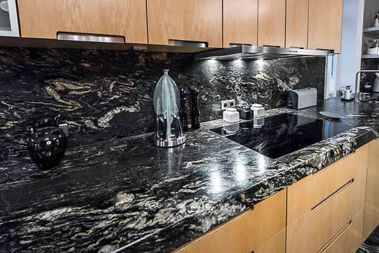 Passgenauer Zuschnitt des Wandbelags aus Granit Black Cosmic zwischen der Küchenarbeitsplatte und den Hängeschränken.